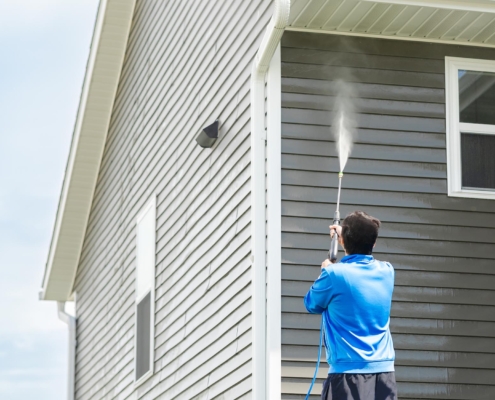 Professional using a power washer on house siding