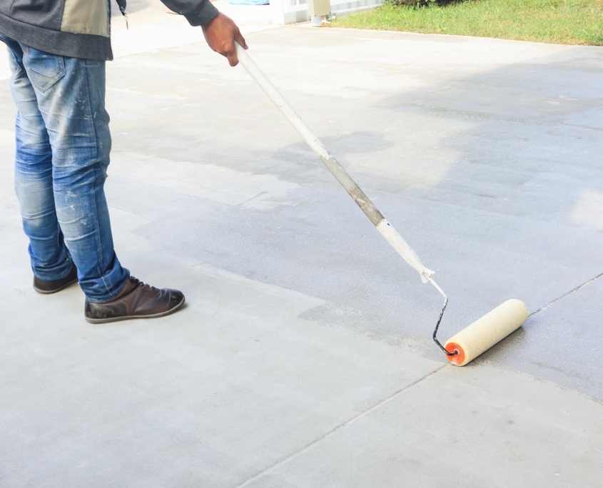 Person using roller to seal concrete driveway