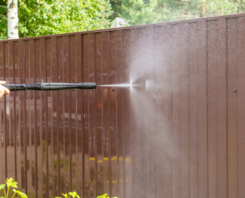 Side view of someone cleaning fence with high pressure power washer